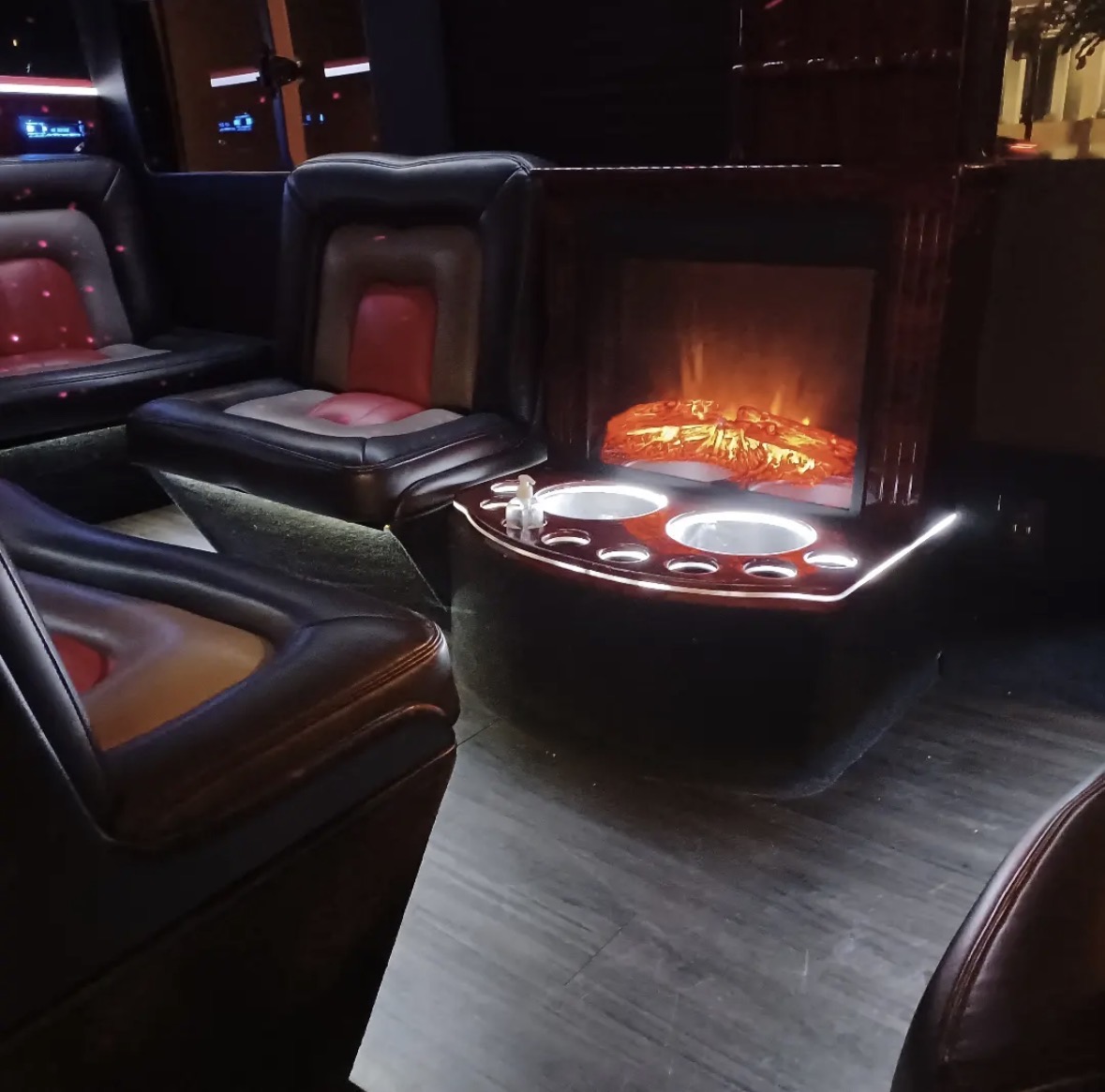 TPL limo Sprinter interior with leather lounge seating, illuminated cup holders, and a fireplace display