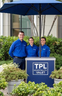 Three TPL valet attendants at an outdoor podium under a blue umbrella